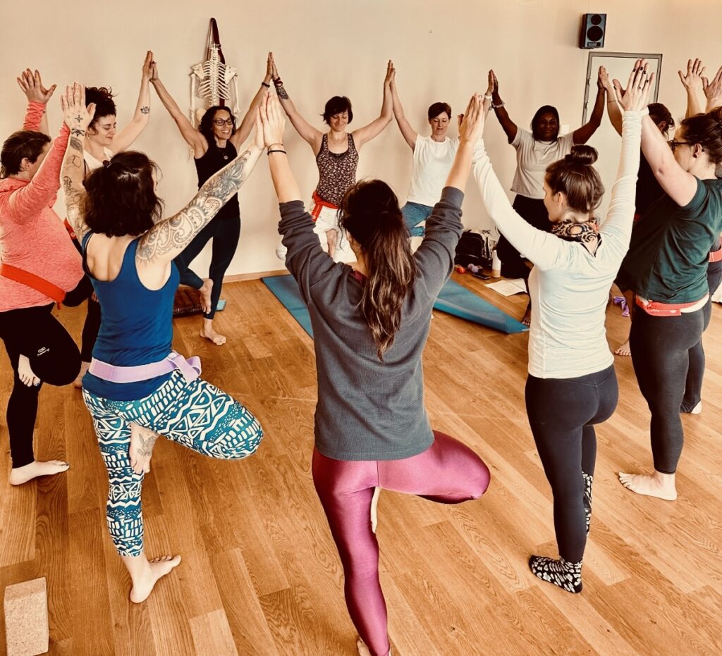 Yogalehrerinnen stehen mit geschlossene Augen im Kreis. Stehen im Asana Baum und ihre Hände berühren sich.